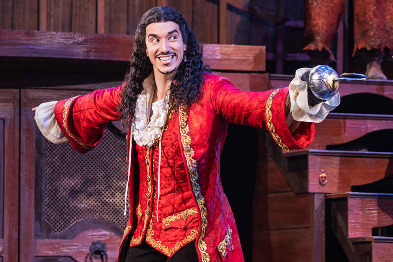 Cody Garcia as Captain Hook in Peter Pan. Captain Hook, donning his signature red jacket and vest, points his hook out in a sort of “en garde” fashion.